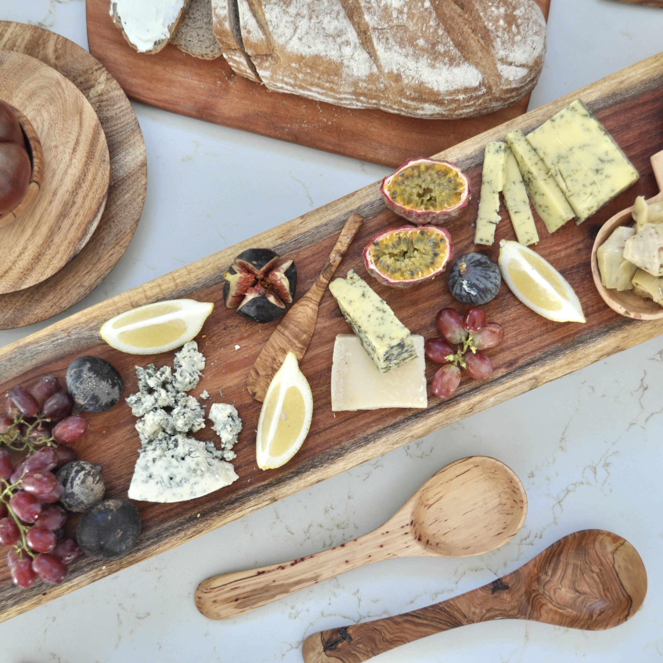 A long wooden serving platter laid with cheese, figs, grapes and bread